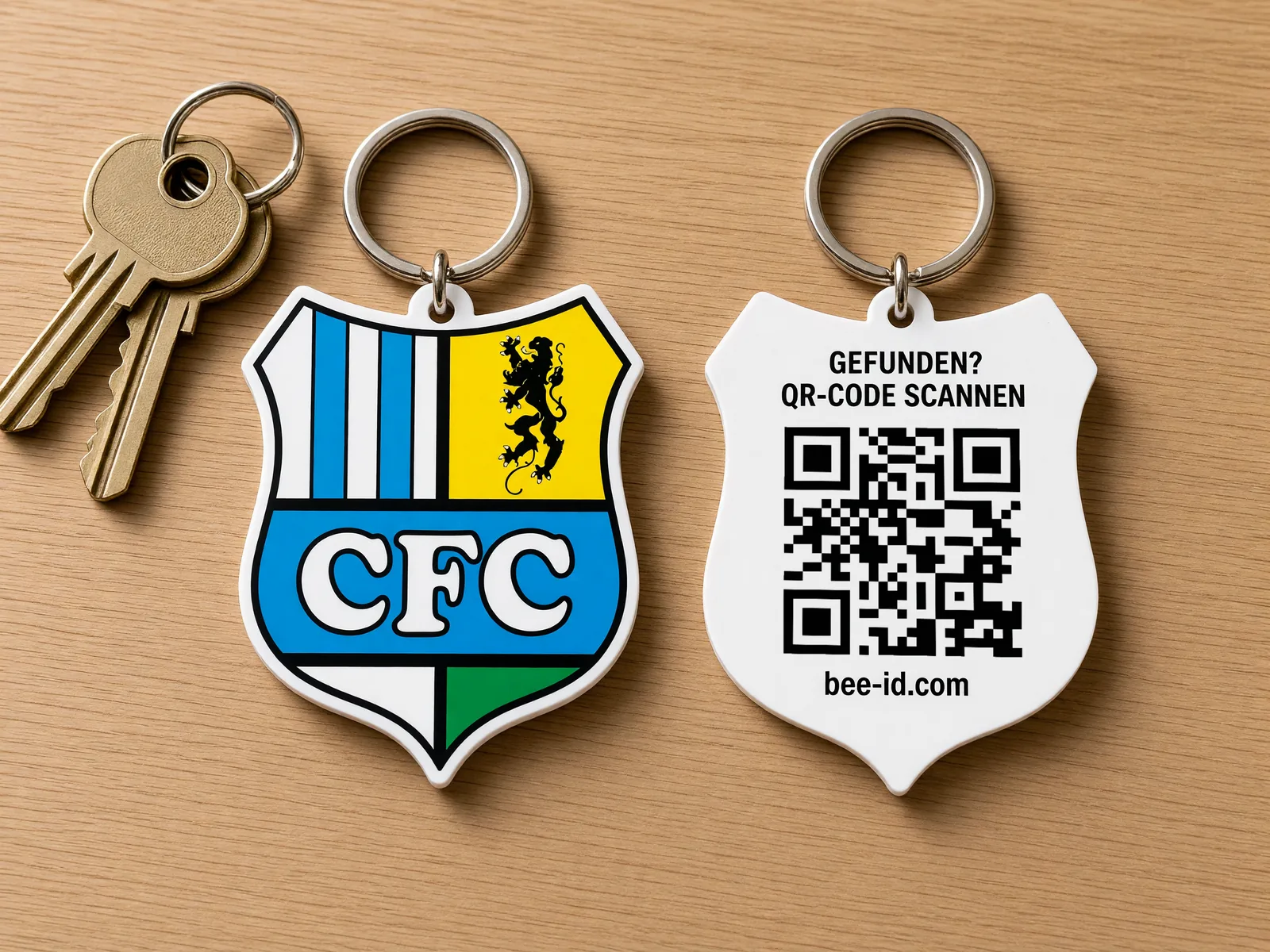 Zwei Schlüsselfundmarken in der Wappenform des Chemnitzer FC: links die Vorderseite mit farbigem Vereinswappen, rechts die Rückseite mit Bee-ID-QR-Code und dem Hinweis „Gefunden? QR-Code scannen“